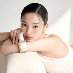 posando con el productoModelo con piel luminosa usando Mixsoon Bean Essence, essence K-beauty minimalista con fermentado de bean para efecto glass skin y tono de piel uniforme